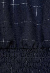 Mörkblått tyg med rutmönster och vita linjer. Textilen har en samlad nederkant med en rynkad elastisk detalj.