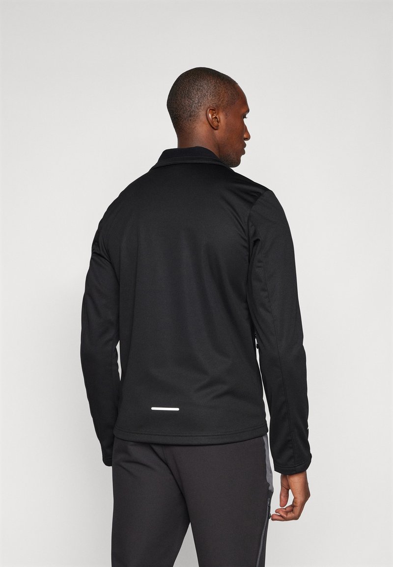 Schwarze Sportjacke mit strukturiertem Finish, Kragen und reflektierendem Akzent auf der Rückseite. Kombiniert mit dunklen Hosen, hat lange Ärmel.