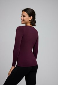 Blusa de manga larga en tejido burdeos oscuro, con un diseño ajustado y textura suave, combinada con leggings negros.