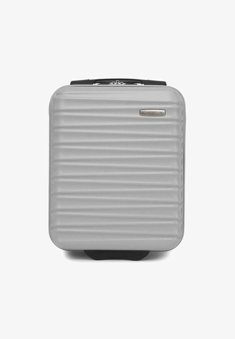 Valise rigide argentée avec une texture à nervures verticales, des bords arrondis et une poignée noire. Présente une plaque de logo sur l'avant. Design compact.