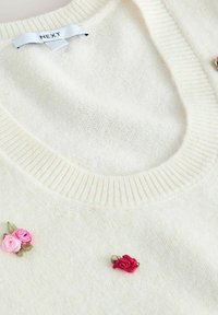 Cremefarbener Pullover aus weichem, strukturiertem Stoff. Verfügt über einen gerippten Halsausschnitt und drei bestickte Rosenakzente in Pink und Rot.