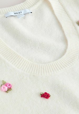 Cream-colored sweater made of soft, textured fabric. Features a ribbed neckline and three embroidered rose accents in pink and red.
