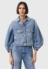 Giacca di jeans con design cropped, colore azzurro chiaro, due tasche sul petto e polsini elasticizzati per un effetto arricciato.