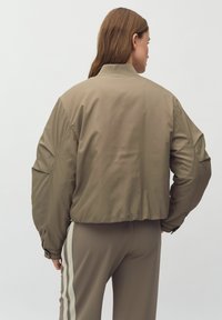 Olivgrön bomberjacka med en kortad design, ribbad krage och elastiska manschetter, med slät, lättviktig tyg och minimal sömnad.