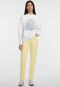Sudadera blanca con un diseño gráfico colorido, combinada con pantalones amarillos claros y zapatillas beige. Tejido suave, corte relajado, estilo simple.