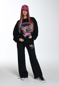 Felpa nera con un design grafico colorato, pantaloni sportivi neri abbinati e un berretto rosa con decorazioni. Tessuto texturizzato e taglio rilassato.