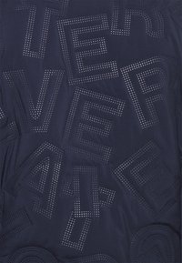 Tecido azul-marinho com letras e números geométricos perfurados. O design inclui formas variadas, com acabamentos metálicos formando padrões.