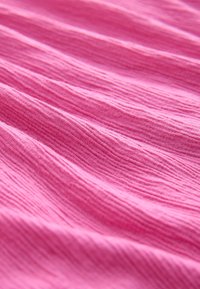 Lyserødt stof med en tekstureret, bølget overflade, der har subtile variationer i farve og mønster, designet for blødhed og fleksibilitet.