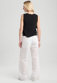 Black knitted sleeveless top with a unique back design, paired with white textured wide-leg pants featuring eyelet patterns and accents.