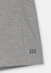 Tissu gris texturé en gros plan montrant un ourlet avec un petit logo "PB" gris foncé imprimé près du bord inférieur.