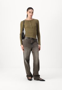 Oliven langermet topp med knapppynt, kombinert med høyt liv svarte gradient jeans og spisse svarte leppestifter, med en liten svart veske.