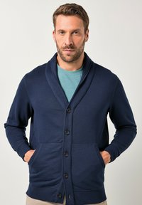 Tmavě modrý kardigán s šálovým límcem, s předním zapínáním na knoflíky, dvěma postranními kapsami a žebrovanými manžetami na rukávech a lemu.