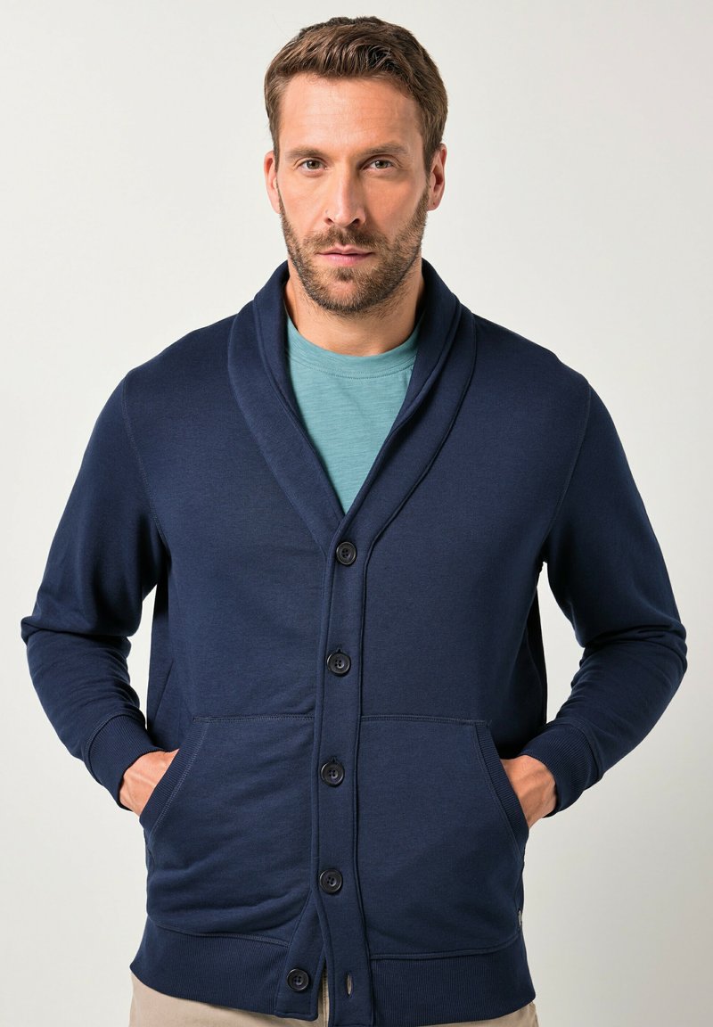 Tmavě modrý kardigán s šálovým límcem, s předním zapínáním na knoflíky, dvěma postranními kapsami a žebrovanými manžetami na rukávech a lemu.