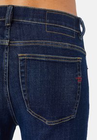 Vaqueros de mezclilla azul oscuro con costuras amarillas, que cuentan con bolsillos traseros y un pequeño detalle en rojo cerca de la cinturilla. Diseño clásico de cinco bolsillos.