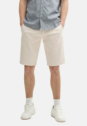Beige Baumwollshorts, gerader Schnitt, knielang, mit seitlichen Taschen und glatter Textur, kombiniert mit weißen Sneakers und Crew-Socken.