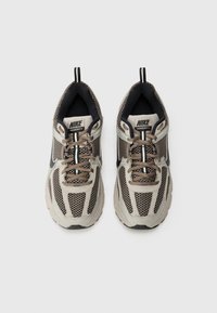 Baskets Nike Vomero 5 en beige clair avec des accents marron, présentant une tige en mesh respirant, un doublure noire, un bout rond et une semelle épaisse.