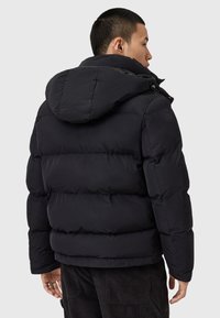 Zwarte pufferjack met capuchon, voorzien van een gewatteerd ontwerp, ritssluitingdetails op de kraag en elastische manchetten voor extra warmte.