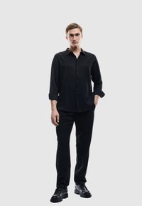 Sort skjorte med lange ærmer, parret med sorte bukser og sorte sko. Glat tekstur, afslappet pasform, minimalistisk design.