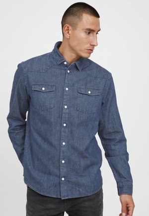 Mørkeblå denimskjorte med knapp-til-ned krage, lange ermer og to brystlommer. Har hvite knapper og et strukturert stoff.