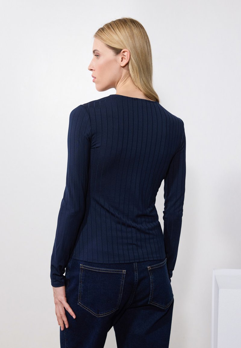 Top blu navy a maniche lunghe a coste con scollatura rotonda, design aderente, tessuto testurizzato, abbinato a jeans in denim scuro.
