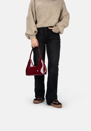 Sac à main en vernis bourgogne avec une forme courbe et une poignée courte, associé à un pull en maille épaisse et un jean noir évasé.