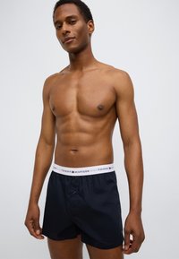 Μαύρα βαμβακερά μποξεράκια με λευκή ελαστική μέση που φέρει το λογότυπο "Tommy Hilfiger". Κλείσιμο με κουμπιά μπροστά και κλασική εφαρμογή.