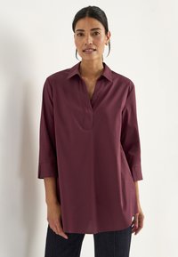 Burgunderfarbene Bluse mit Kragen, V-Ausschnitt und dreiviertel Ärmeln, aus glattem Stoff, mit lockerem Schnitt und seitlichen Schlitzen.