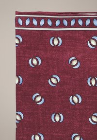 Bordowa tkanina z wzorem niebieskich i beżowych okrągłych kształtów, obramowana niebieskim wzorem liści, o teksturowej powierzchni i gładkim wykończeniu.