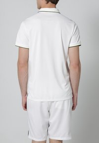 Biała koszulka polo w slim fit, z wąskim czarnym i zielonym kołnierzykiem, krótkimi rękawami oraz gładką fakturą. Widoczna metka na dolnym skrawku.