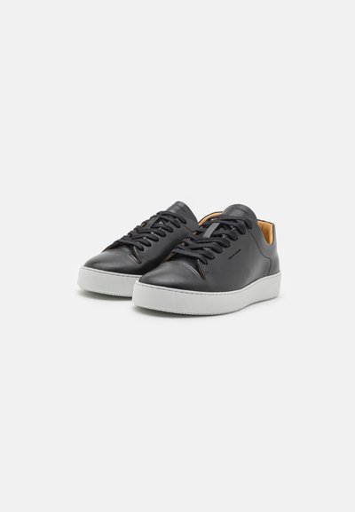 Sapatilhas em couro preto com design de atacadores, sola de borracha branca e detalhes interiores em tom de pele. Textura suave e estilo minimalista.