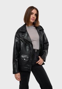 Černá kožená moto bunda s nýty na ramenou a rukávech, se zipovými kapsami a mírně oversized střihem.