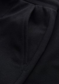 Close-up of a black garment pocket made of textured fabric with visible stitching along the edges.