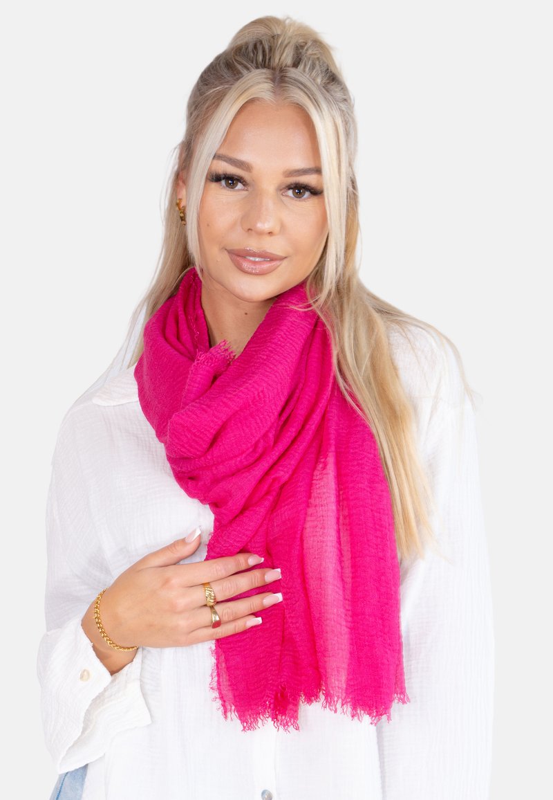 Écharpe fuchsia en tissu léger et texturé, avec des bords à franges, drapée de manière élégante autour du cou.