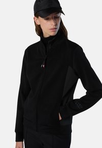 Chaqueta negra con cremallera y una textura suave, con un cuello alto, paneles laterales y la marca "NORTH SAILS" en la manga.