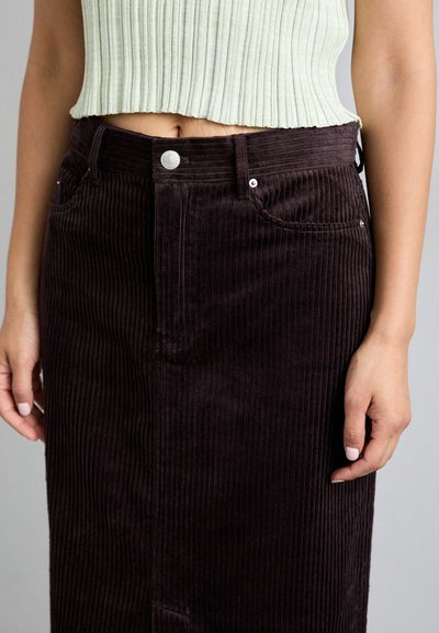 Brun kordfløyelskjørt med vertikale ribber, med frontlommer og knappeåpning. Brukt med en lysegrønn ribbet crop top.