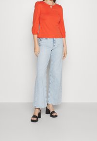 Red, fitted top with three-quarter sleeves, keyhole neckline. Light blue, wide-leg jeans, frayed hem. Black platform sandals with wide straps.