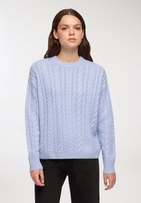 Jasnoniebieski sweter dzianinowy z wzorem w warkocze, okrąg�łym dekoltem i długimi rękawami, stylizowany z czarnymi spodniami.