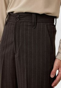 Bruine gestreepte broek met een knoopsluiting met twee knopen, riemlussen en zijzakken. De stof textuur lijkt glad en zorgvuldig vervaardigd.