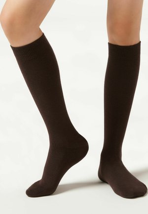 Knähöga bruna strumpor gjorda av ett slätt, elastiskt material med ribbade muddar och rundad tådesign.