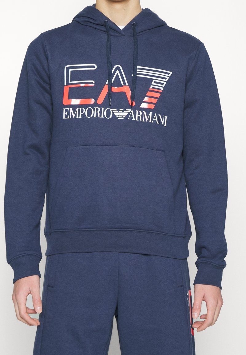 Marinblå hoodie i mjukt tyg, med en framficka i kängurustil, dragsko-huva och en djärv kontrasterande logotryck över bröstet.