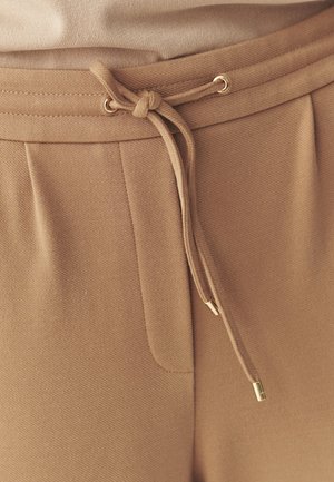 Beige joggers met een trekkoord in de taille, voorzien van gouden accenten en een textuurstof. Inclusief zijzakdetails.