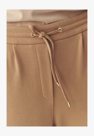Beige joggers with a drawstring waistband, featuring gold-tone accents and textured fabric. Includes side pocket detail.