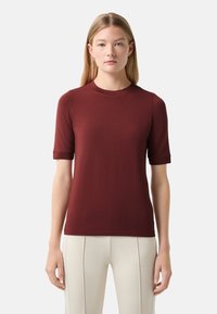 Burgundy short-sleeve t-shirt with a round neckline and a smooth, soft texture. Fitted shape with rolled sleeves.