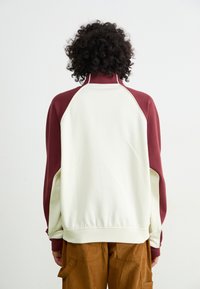 Pullover with a high collar, featuring a maroon top section and cream lower section. Soft fabric with ribbed cuffs and hem.