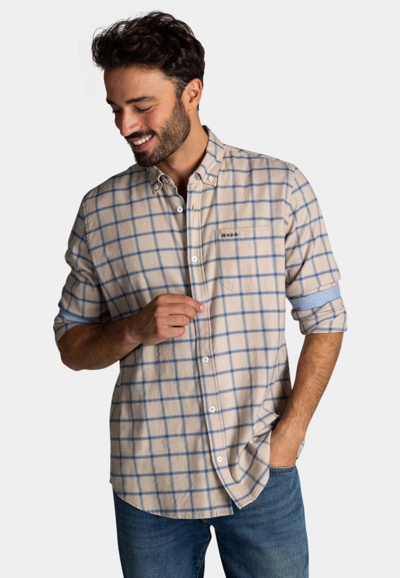 Geruite beige blouse met blauwe ruitjes; zachte textuur, met opgerolde lange mouwen, één borstzak, witte knopen.