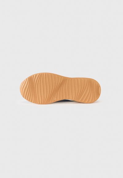 Podešev boty z světle hnědé gumy s vlnitou texturou a detailními drážkami; hladké okraje zužující se u špičky a paty.