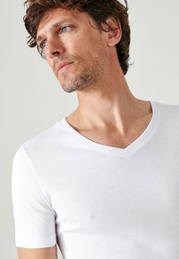 White V-neck T-shirt made from soft cotton, featuring short sleeves and a slim fit. Smooth texture with minimal seams and detailing.