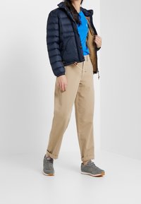 Námořnická prošívaná bunda s vodorovnými pruhy, béžové kalhoty a šedé tenisky. Bunda má kapuci a přední zip s kapsami.