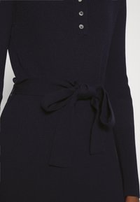 Marinblå ribbad stickad klänning med lång ärm, försedd med en rad knappar och ett knytbälte i midjan för en figursydd silhuett.