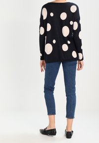 Navy sweater with large cream polka dots, relaxed fit, drop shoulders, paired with slim-fit blue jeans and black loafers.
